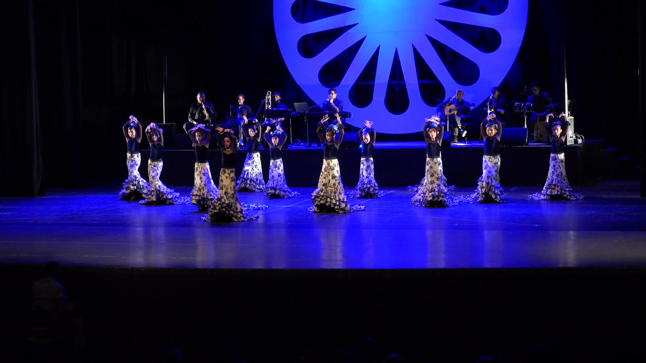 Women dancers on a blue-lit stage with musicians behind them.