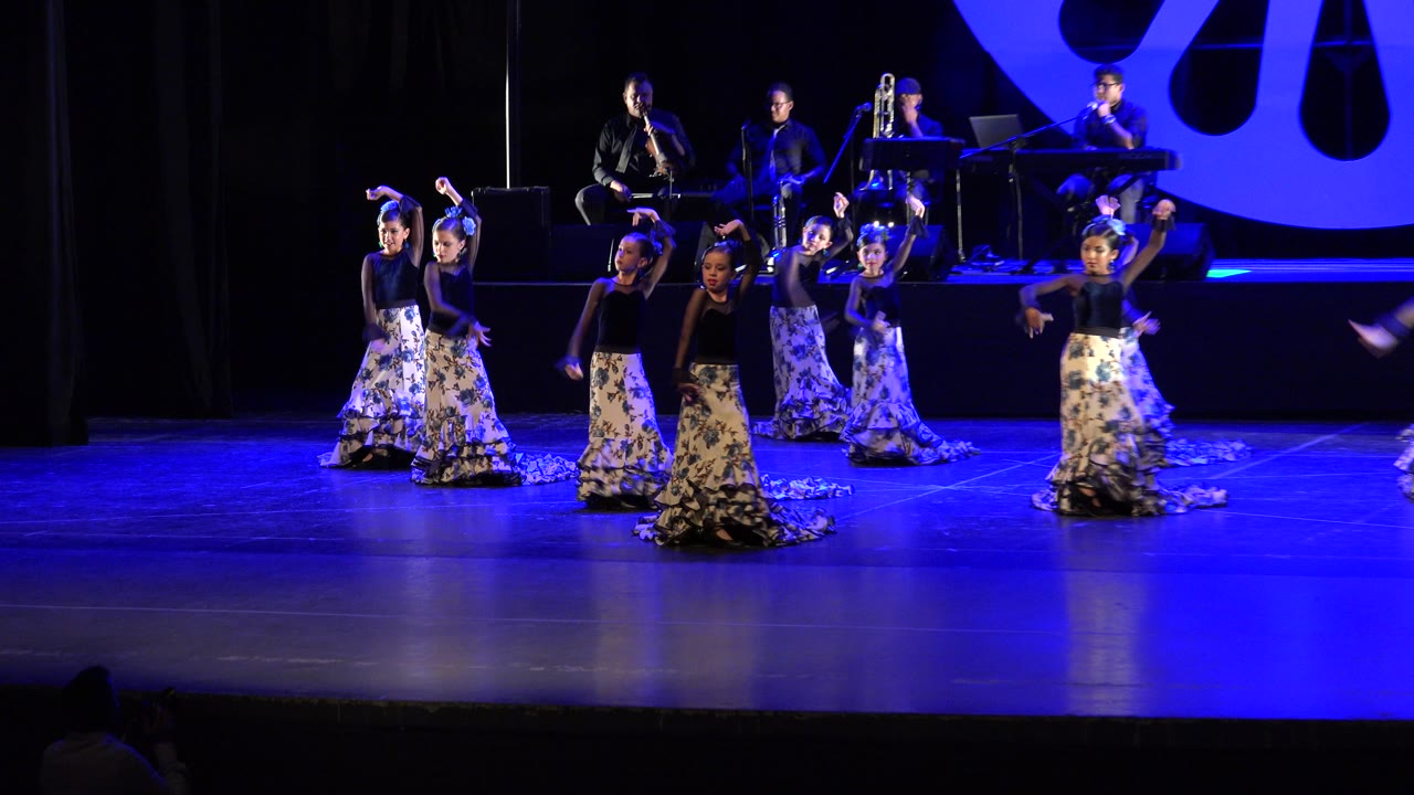 Dancers shifting positions on a stage in front of live musicians.
