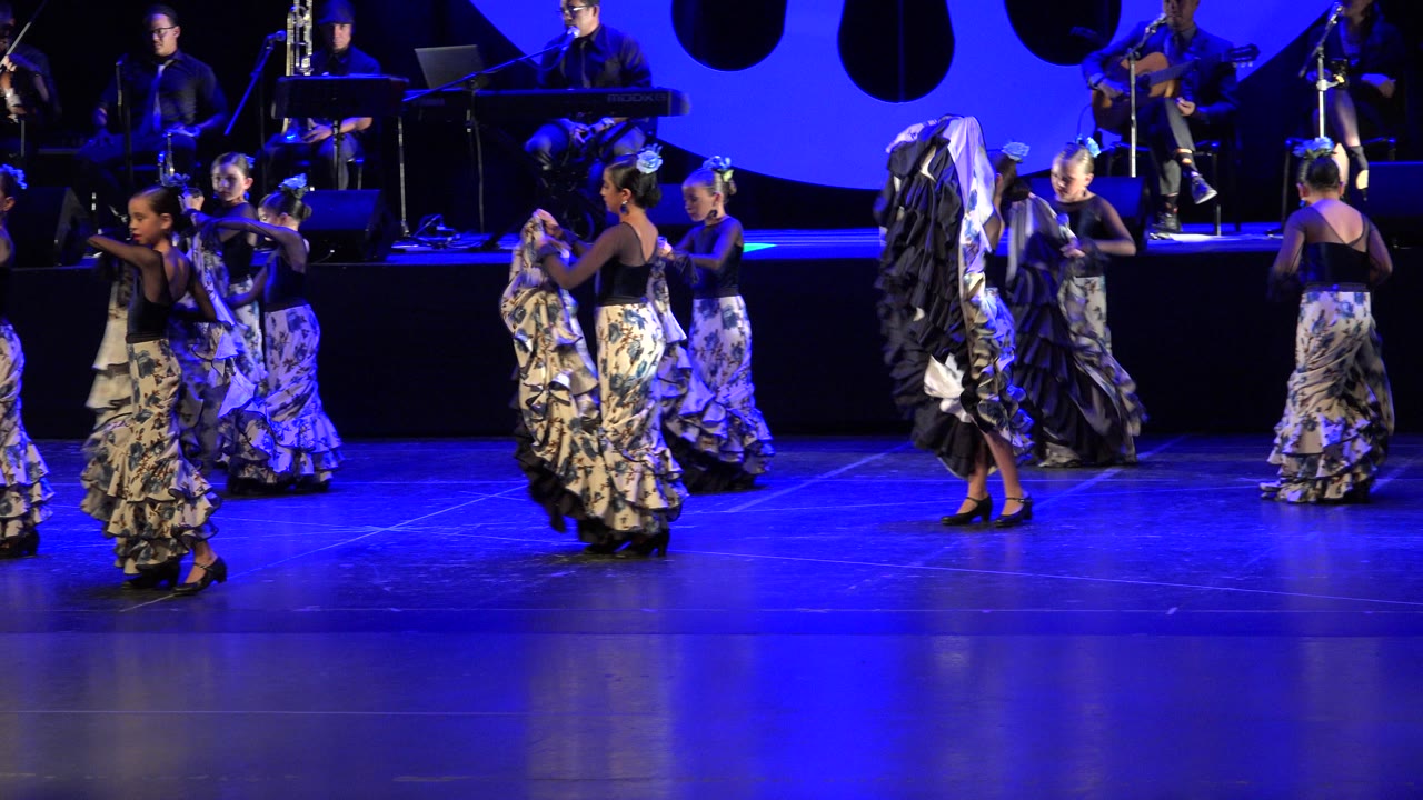 One second into the Cabo San Lucas clip, several children lift and turn their patterned skirts as other dancers continue the routine under strong blue theater light.