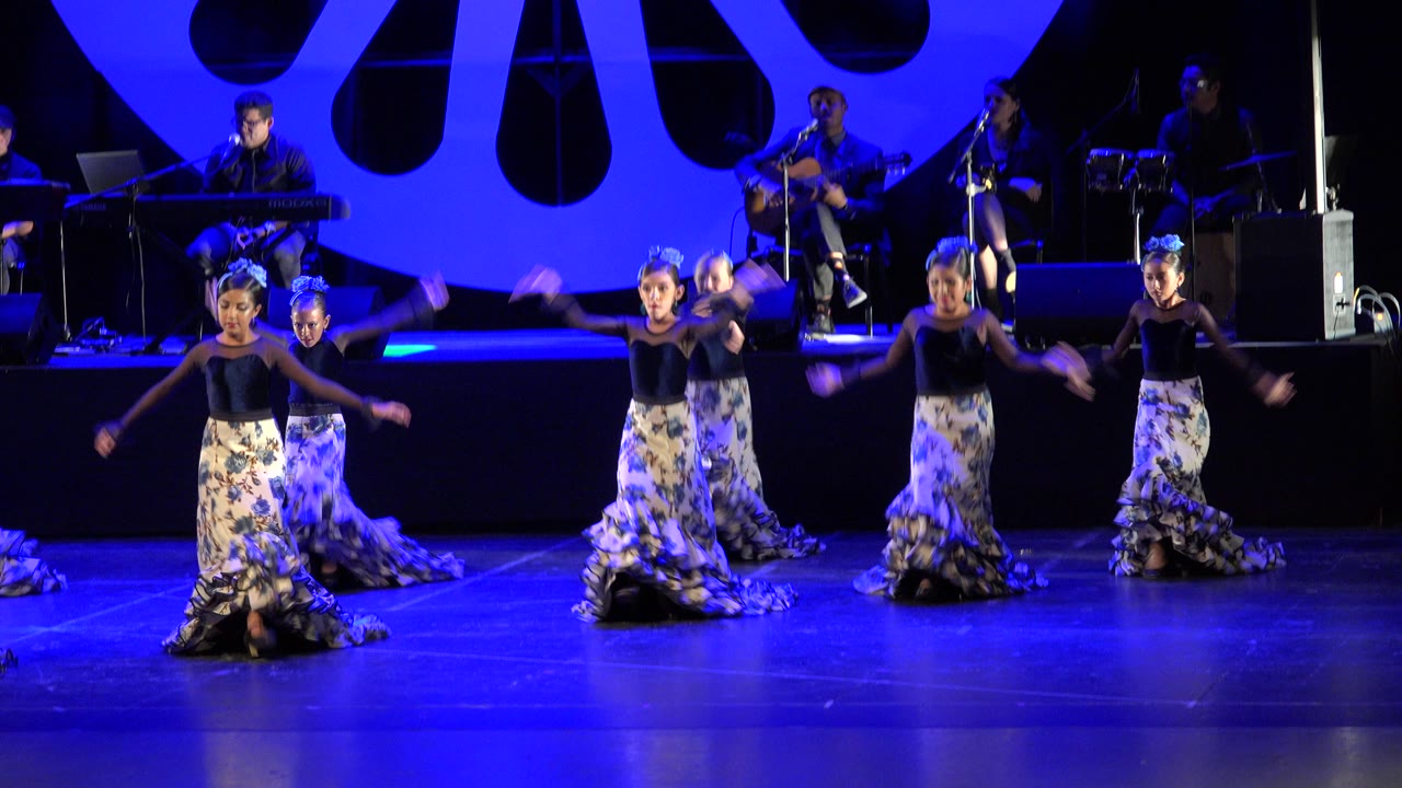 Children dance on a blue-lit stage with musicians behind them.