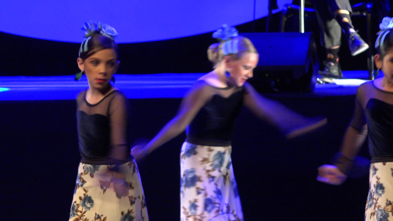The dancers continue the routine in Cabo San Lucas, with one girl facing forward and another moving her arms beside her under the blue wash.