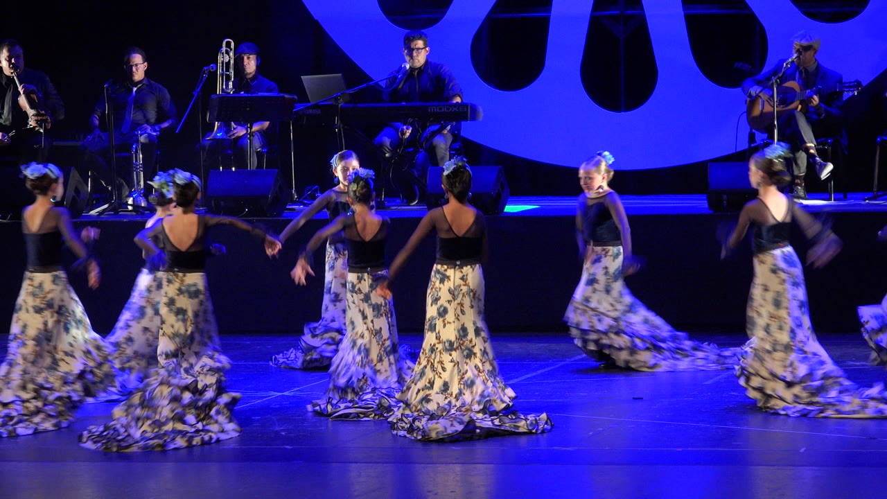 In Cabo San Lucas, Mexico, the dancers shift formation across the blue-lit stage with patterned skirts trailing while musicians remain seated in the rear.