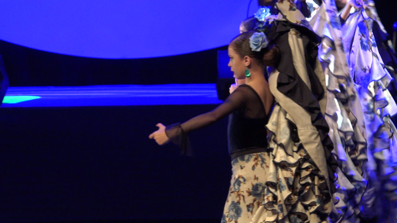 Girl in costume dances beside ruffled fabric on a blue-lit stage.