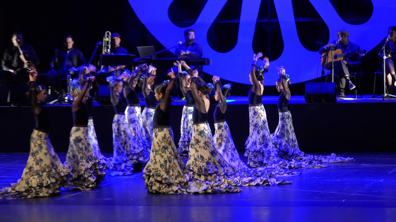 Women dancing on a blue-lit stage with a band behind them.