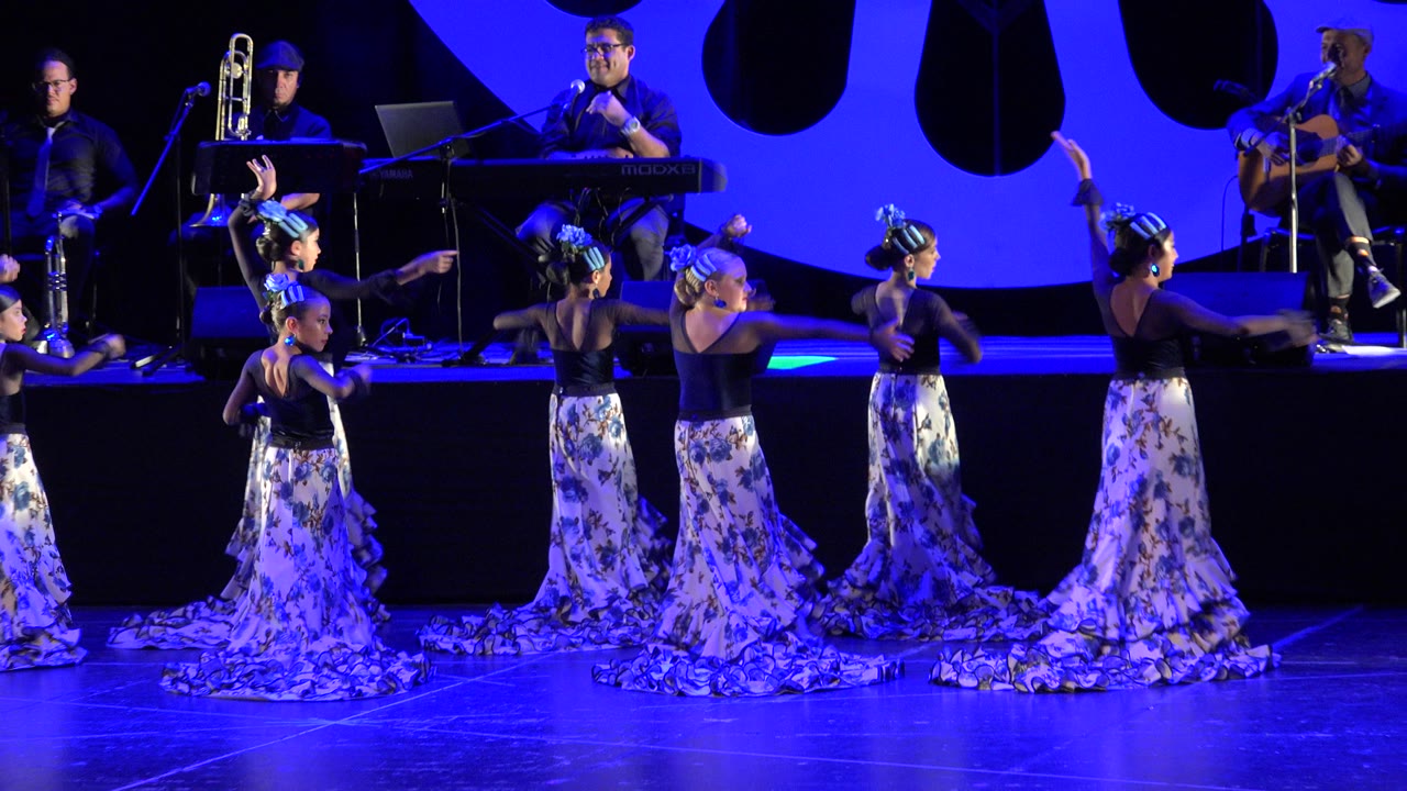 Young girls dancing on a blue-lit stage with musicians behind them.