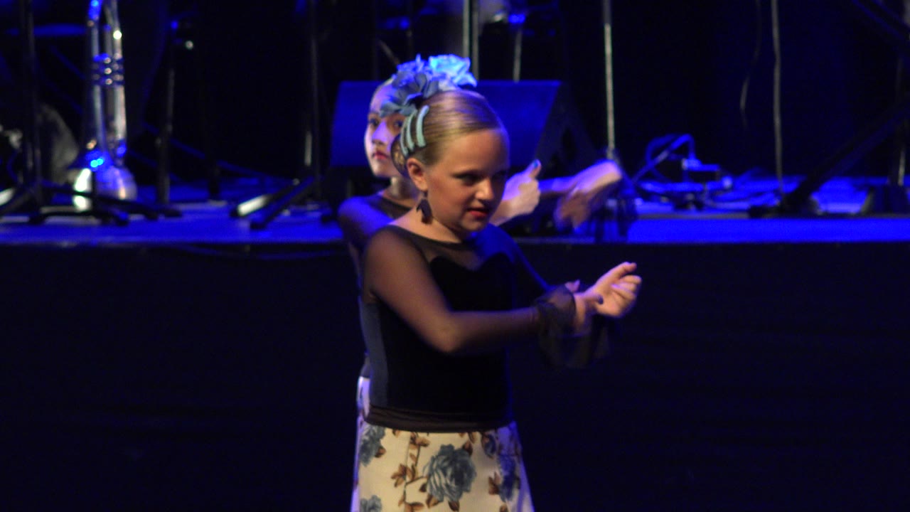The lead girl points her fingers in front of her chest while a second child remains aligned behind her on the dark blue-lit stage in Cabo San Lucas, Mexico.