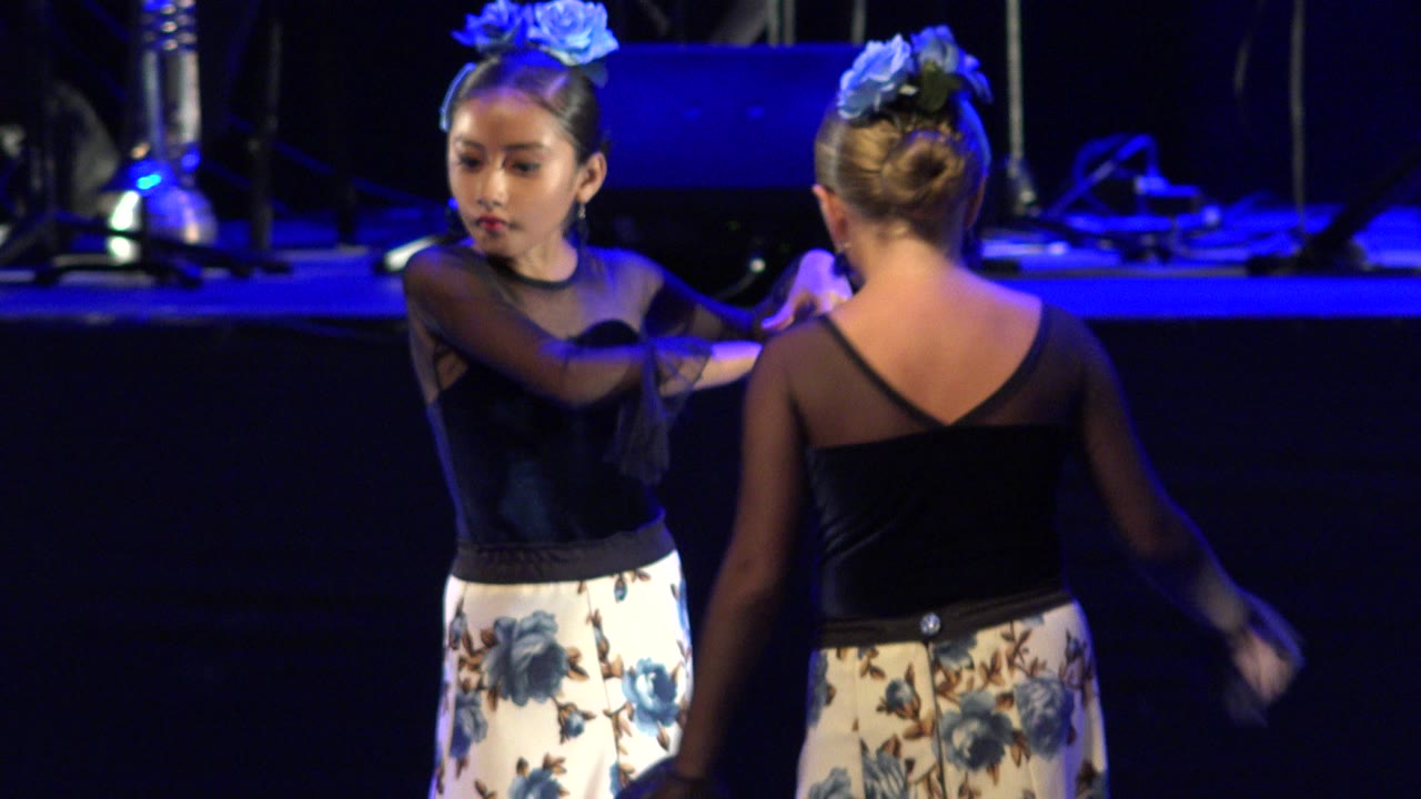 Two young girls in black and white dance costumes face each other on a blue-lit stage.