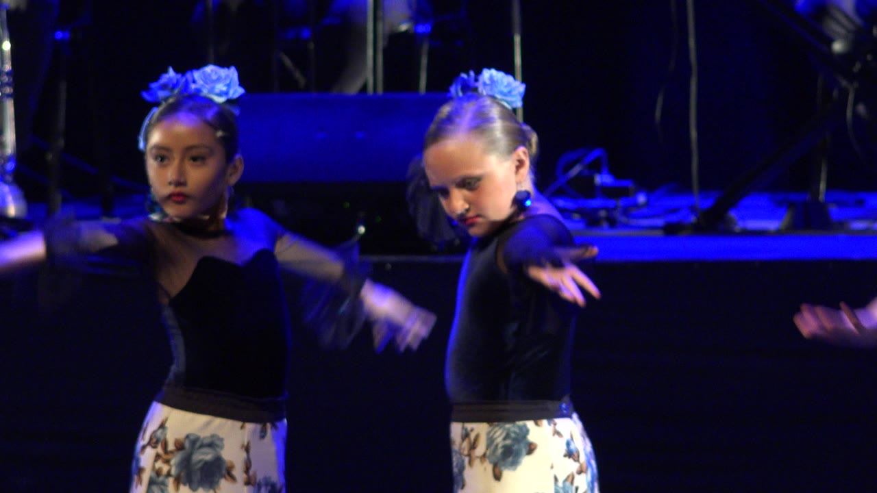 Two girls extend their arms while dancing on stage.