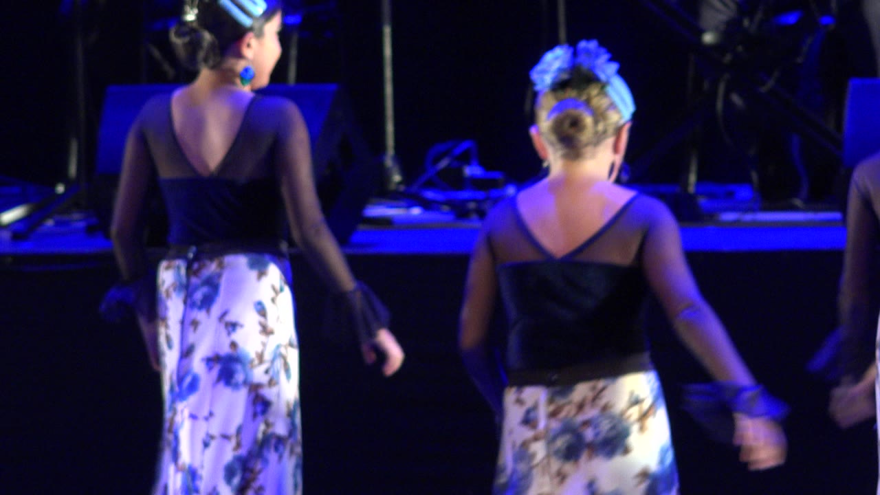 Two young dancers seen from behind on a blue-lit stage.