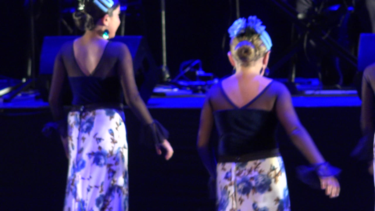 The same pair of young dancers remains back-facing, with arms lowered and blue stage lighting across the performance area in Cabo San Lucas, Mexico.