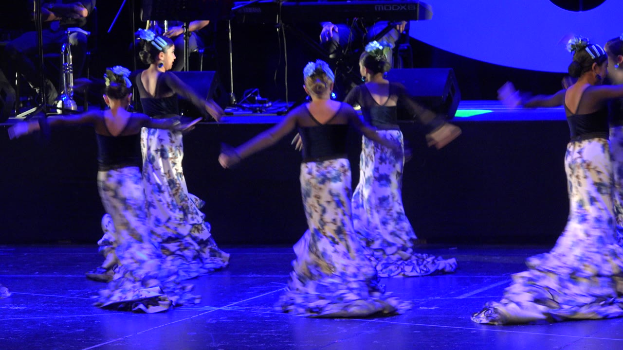 Young girls in floral skirts dancing on a blue-lit stage.