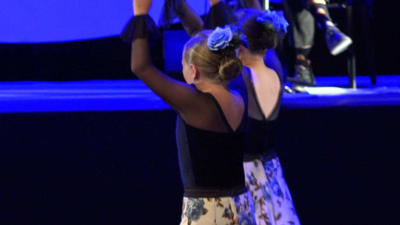 Two young dancers seen from behind on a blue-lit stage.