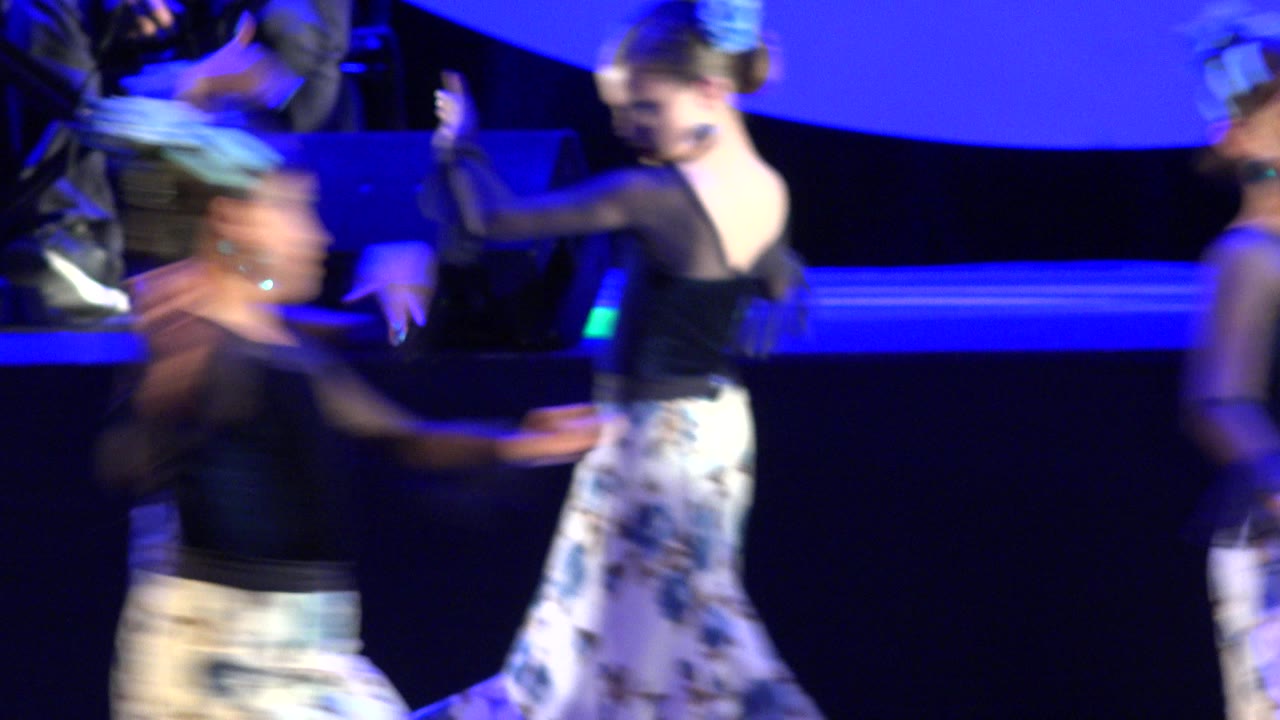 Blurred dancers crossing a blue-lit stage