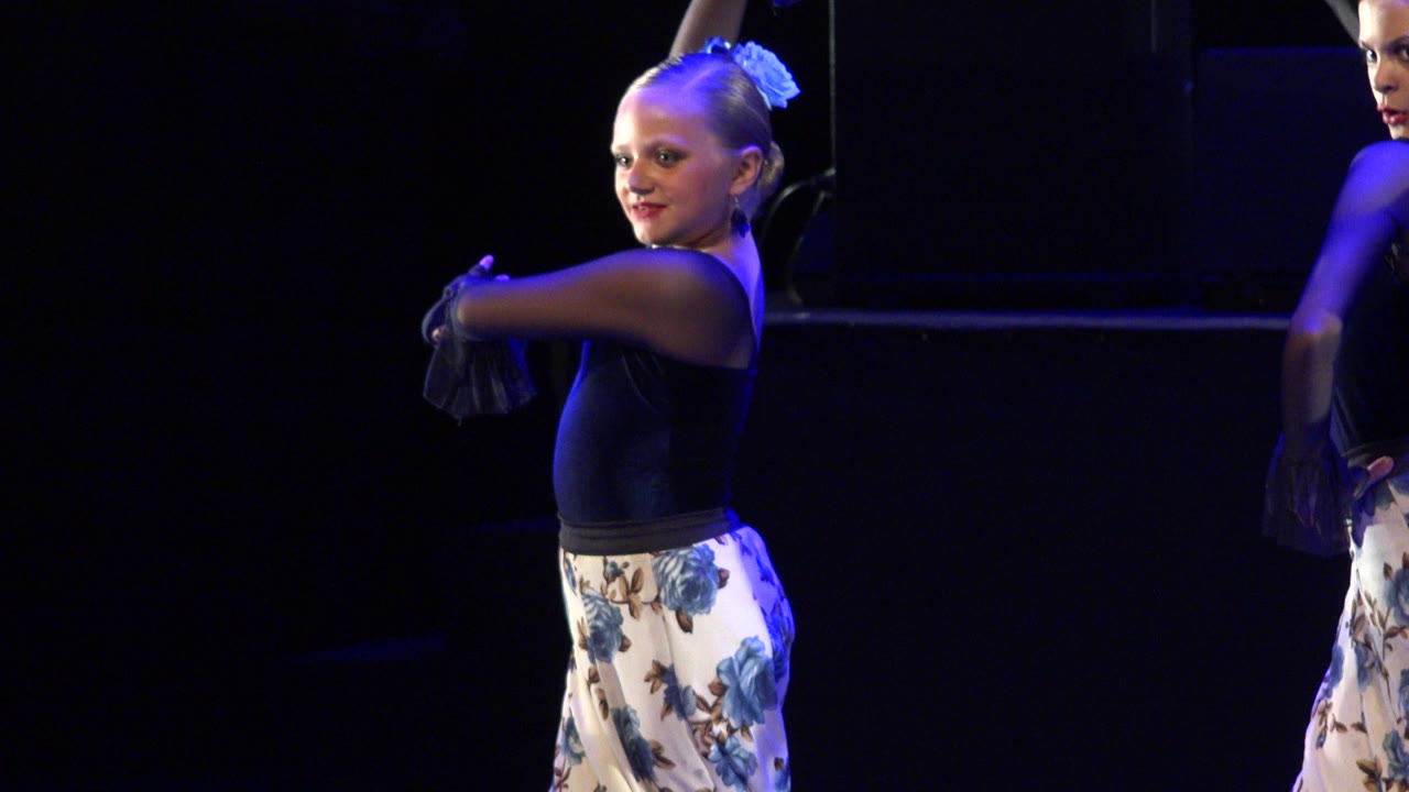 Young dancer smiling on a dark stage with blue light.