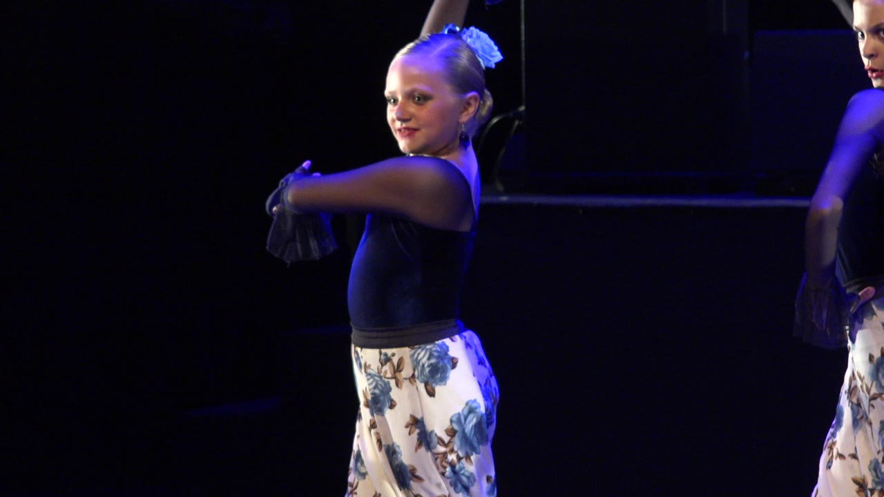 Young female dancer in Cabo San Lucas remains centered in a black top and white floral skirt, with blue light outlining her hair and shoulders.