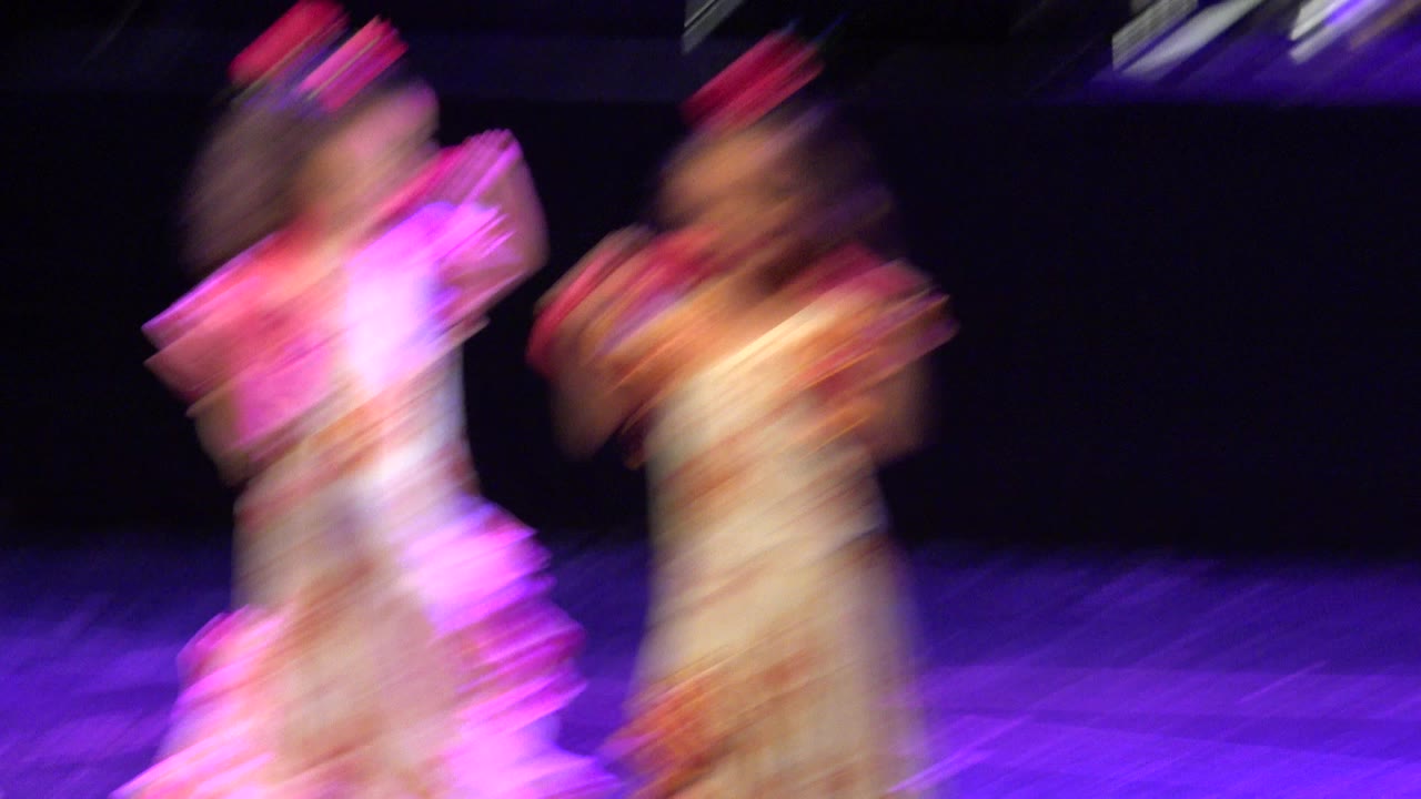 Blurred girls in matching costumes dancing on a purple-lit stage.