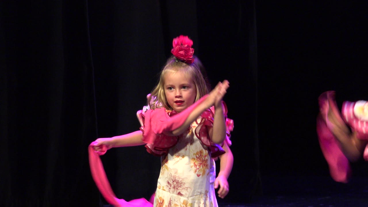 Young girl swings a pink scarf across her body on stage.