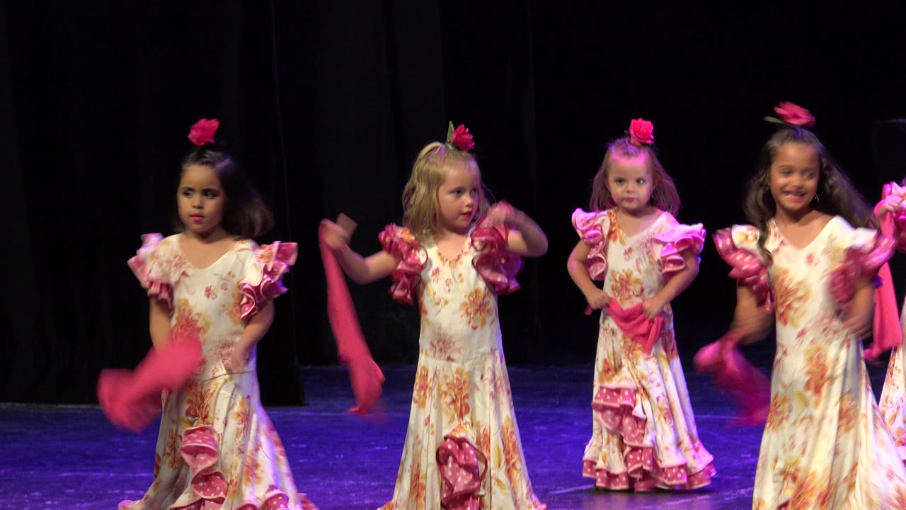 Four young girls in long cream floral dresses dance with pink shawls on a black-curtain stage in Cabo San Lucas, Mexico.