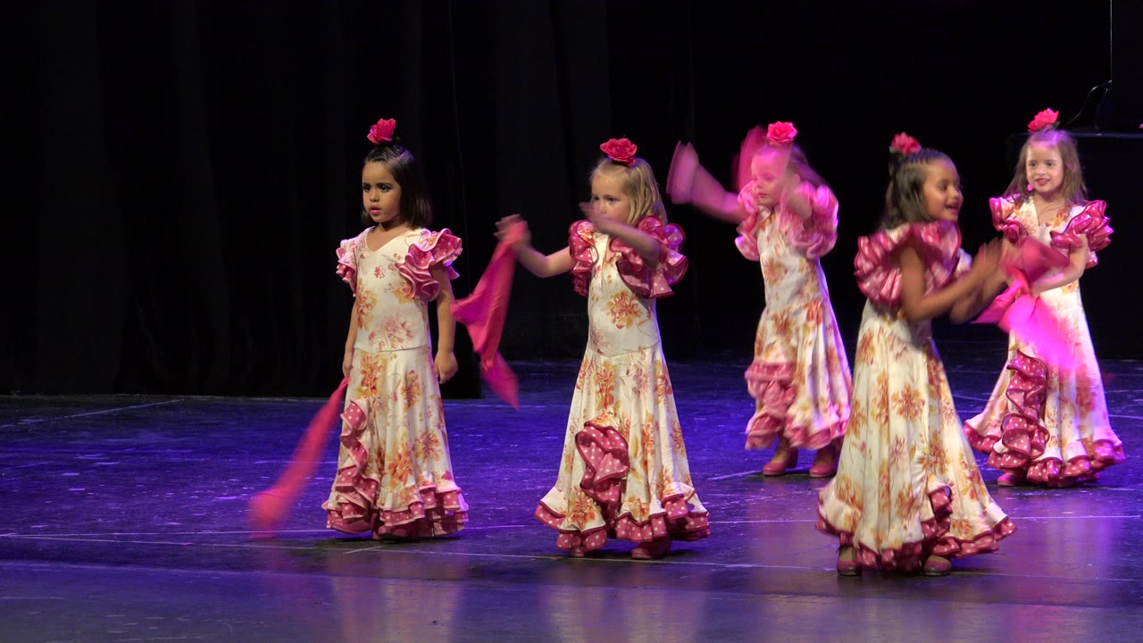Young girls in matching pink and white costumes continue the stage dance in Cabo San Lucas, Mexico, with one scarf blurred as it swings upward.