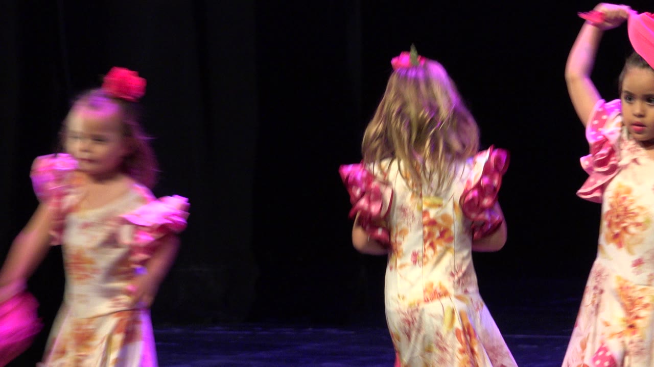 Girls in pink ruffled dance costumes stand near the right side of the stage.
