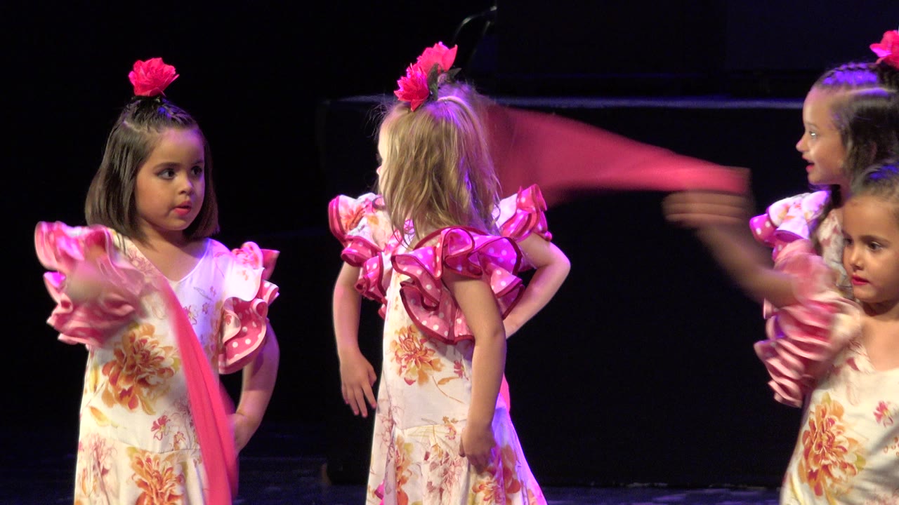 Young girls in floral dance costumes on a dark stage.