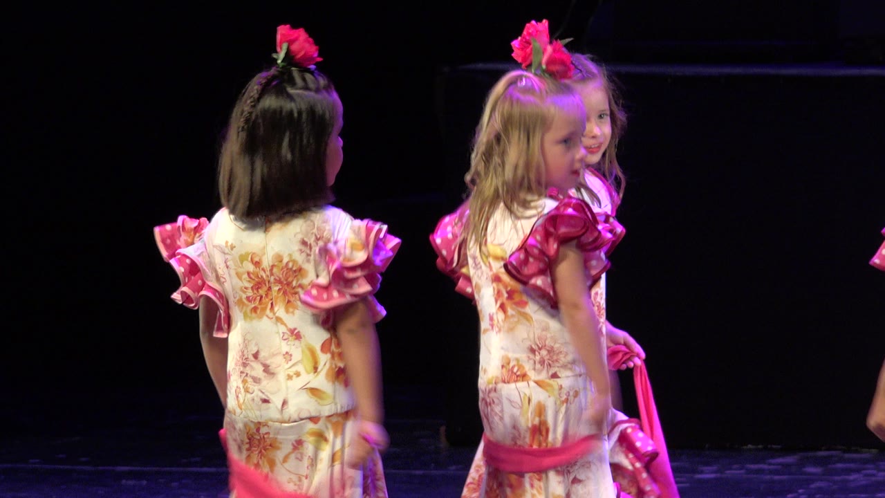At 0:01 in Cabo San Lucas, Mexico, two young girls in matching floral outfits hold bright pink fabric while another child is partly visible behind them.