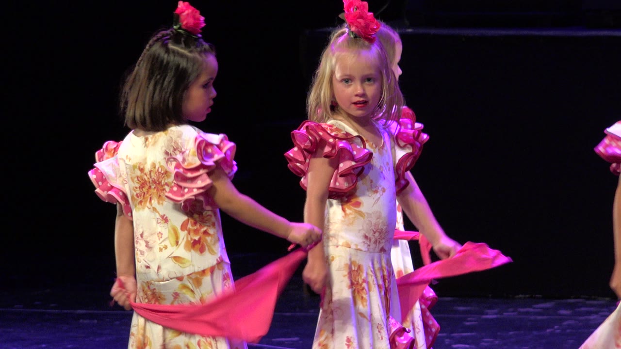 The girls remain near center frame in Cabo San Lucas, Mexico, with one facing the camera and the other turned partly sideways while holding the pink dance fabric.