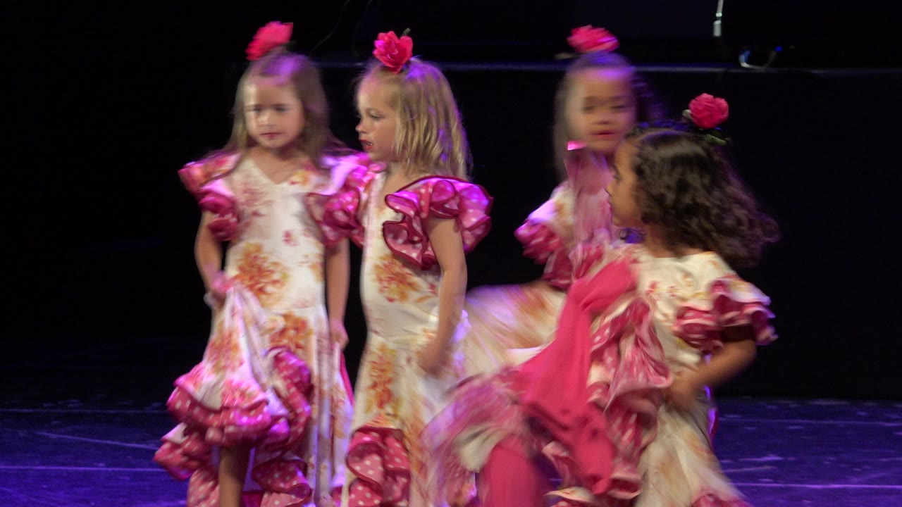 Several young dancers in pink-trimmed floral costumes move across the stage in Cabo San Lucas, Mexico, with one child blurred by motion in the foreground.