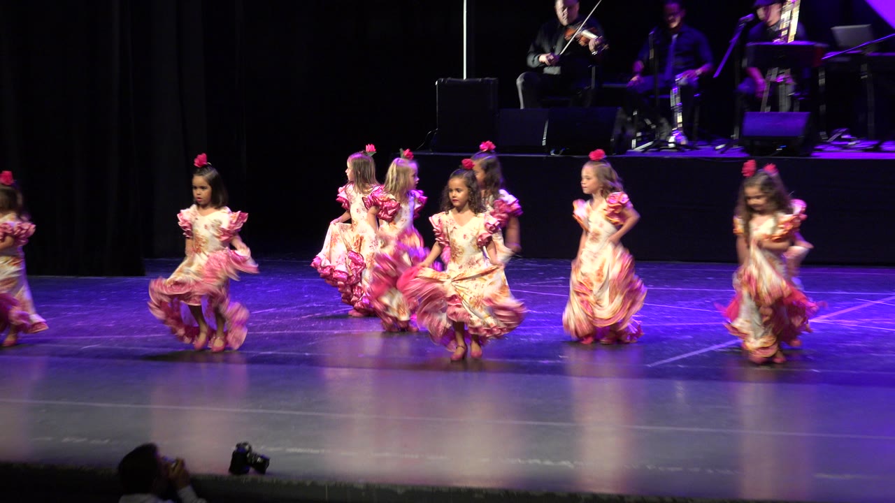 Young girls in pink ruffled dresses dancing on a stage.