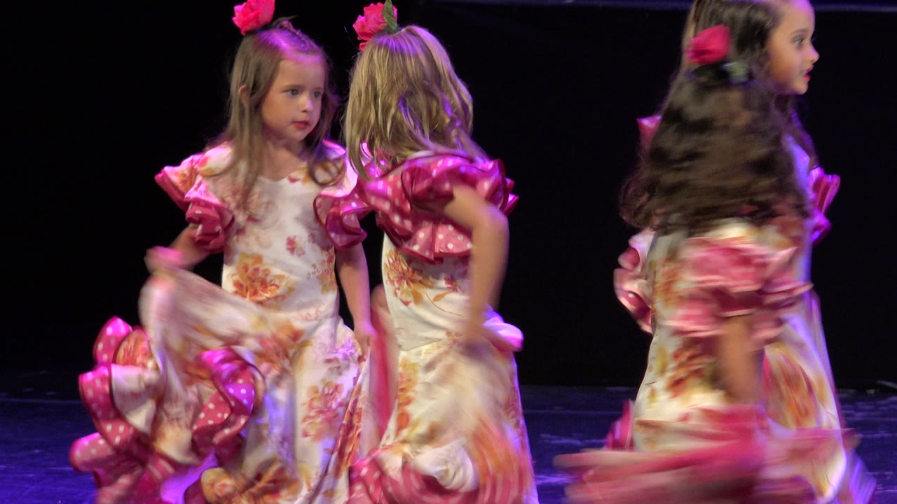 Girls in matching dresses moving across a black stage