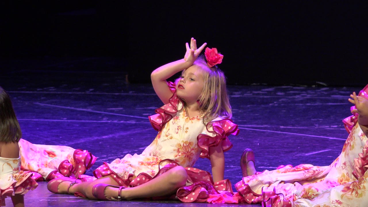 At 0:01, the young girl remains seated in Cabo San Lucas with her legs folded forward, pink costume trim bright against the purple-lit floor and a second child cropped at the right edge.