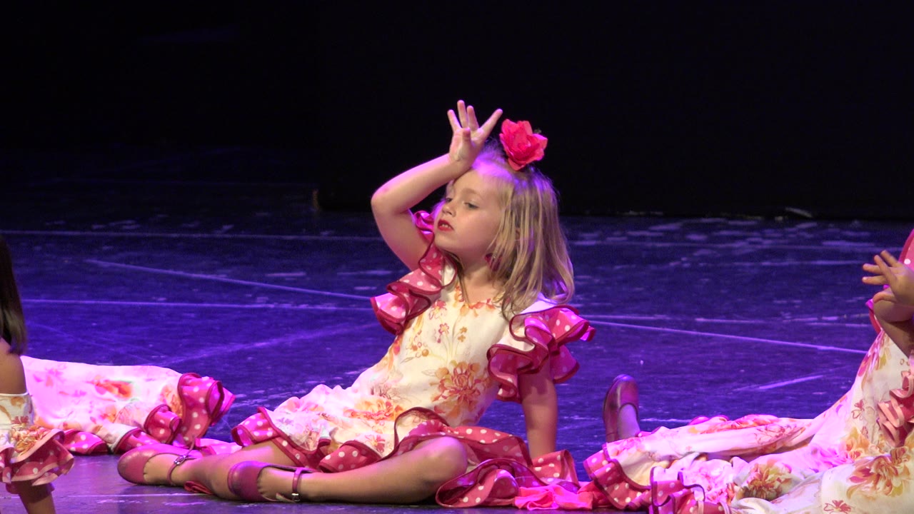 Seated girl in pink and floral costume poses with hand near her face.