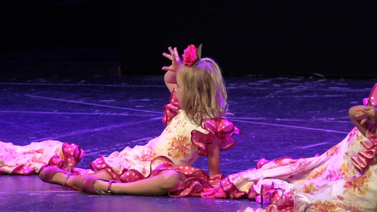 Small girl seated on a stage in a pink and white costume.