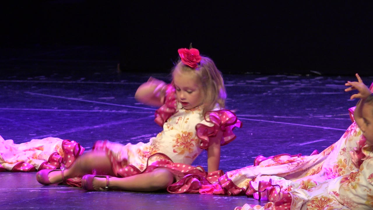 Girl on stage lowering her hand as other children enter the frame.