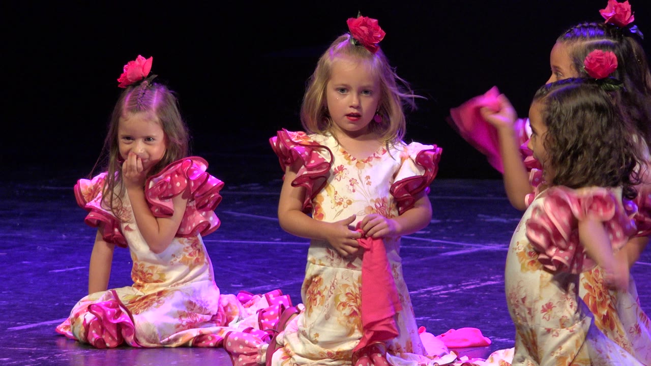Young girls in pink-trimmed dresses on a dark stage.