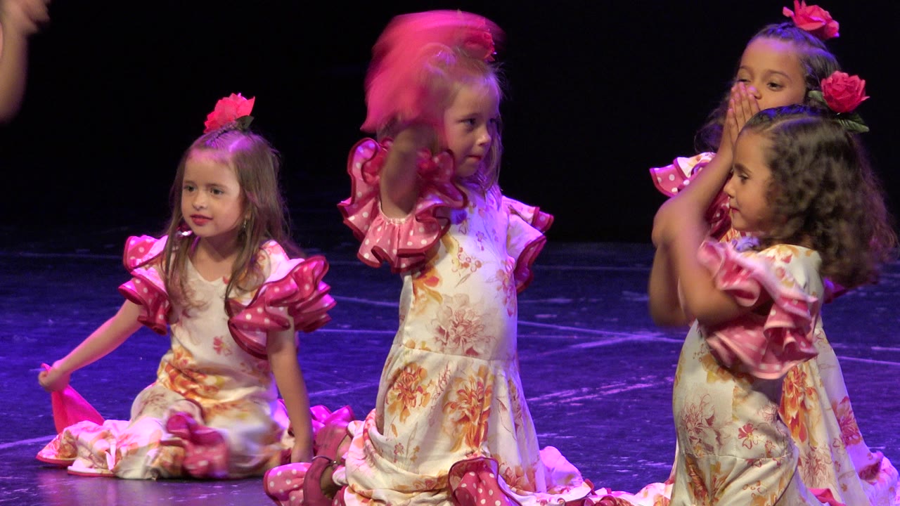 Young girls in pink-accented dresses on a dark stage.