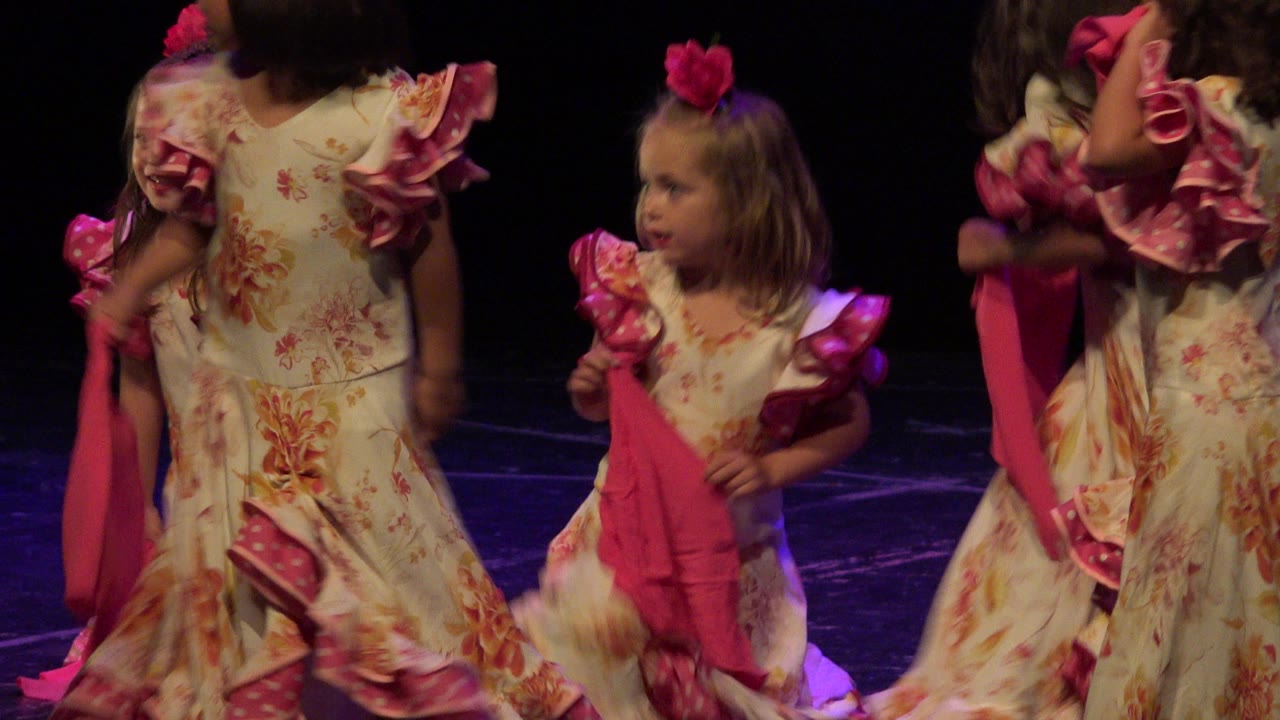 Young girls in floral dresses dancing on a dark stage.