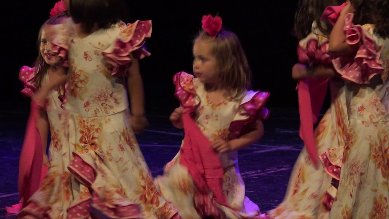 Children in matching floral dresses pass each other under colored stage light during a dance recital in Cabo San Lucas, Mexico.