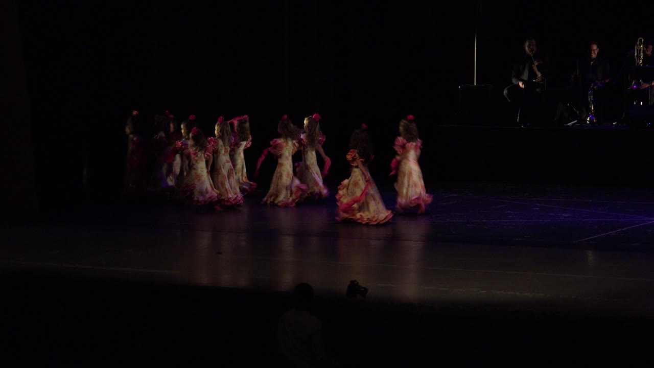 Children in red and white dresses dance on a dark stage.