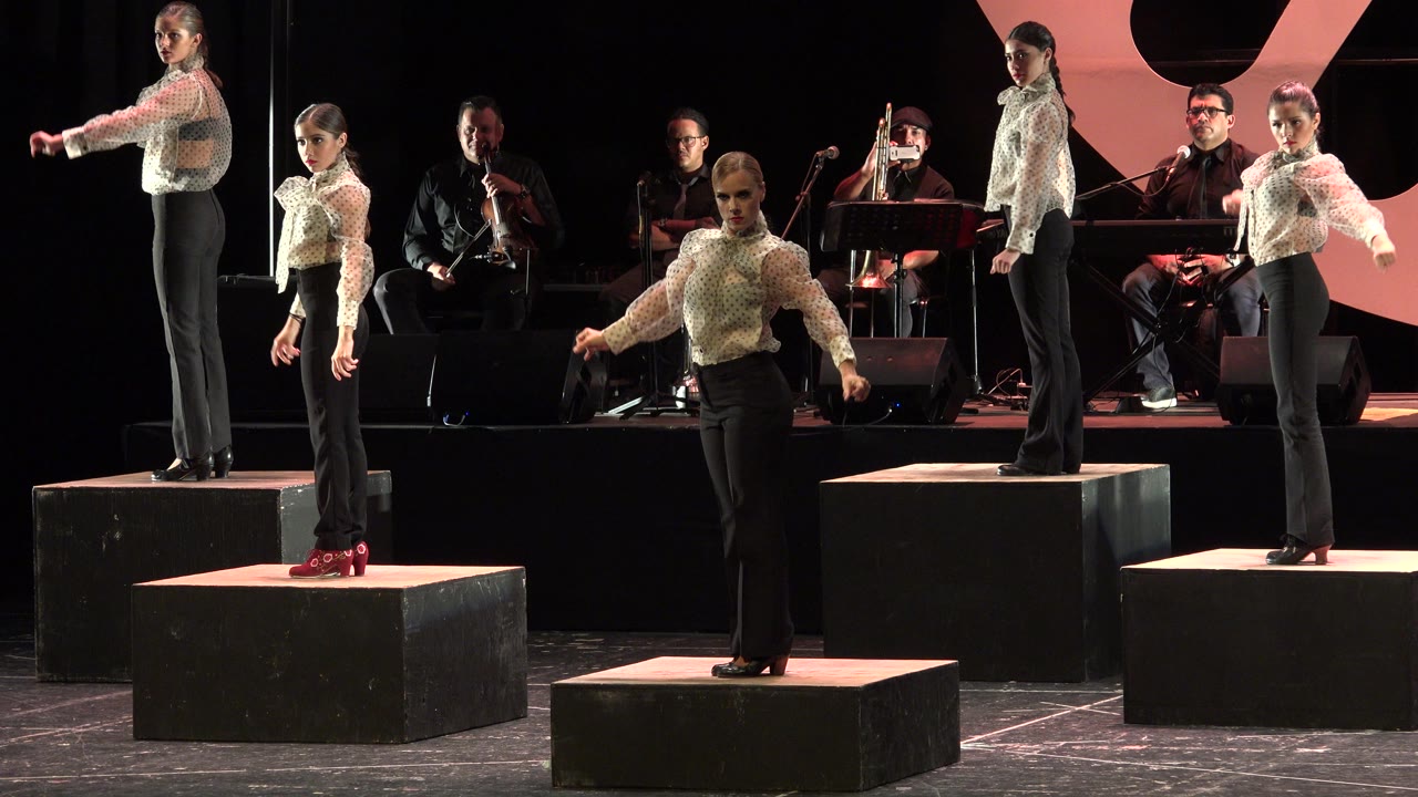 Dancers on black risers with musicians behind them on a dark stage.