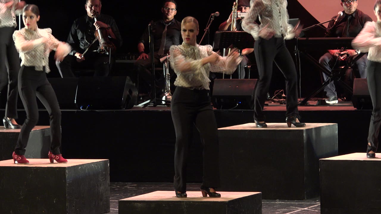 Dancer crossing her arms while standing on a lit black cube.