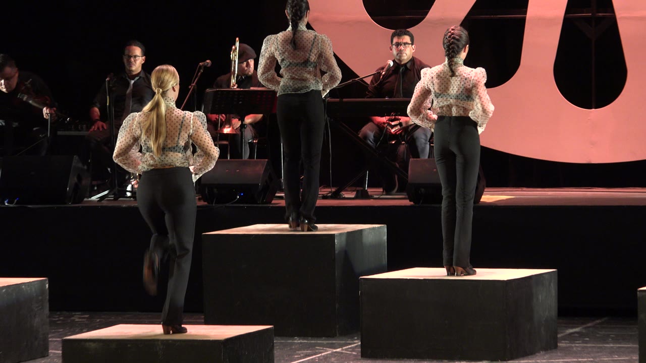 A dancer steps onto a platform while other dancers remain posed across the stage.