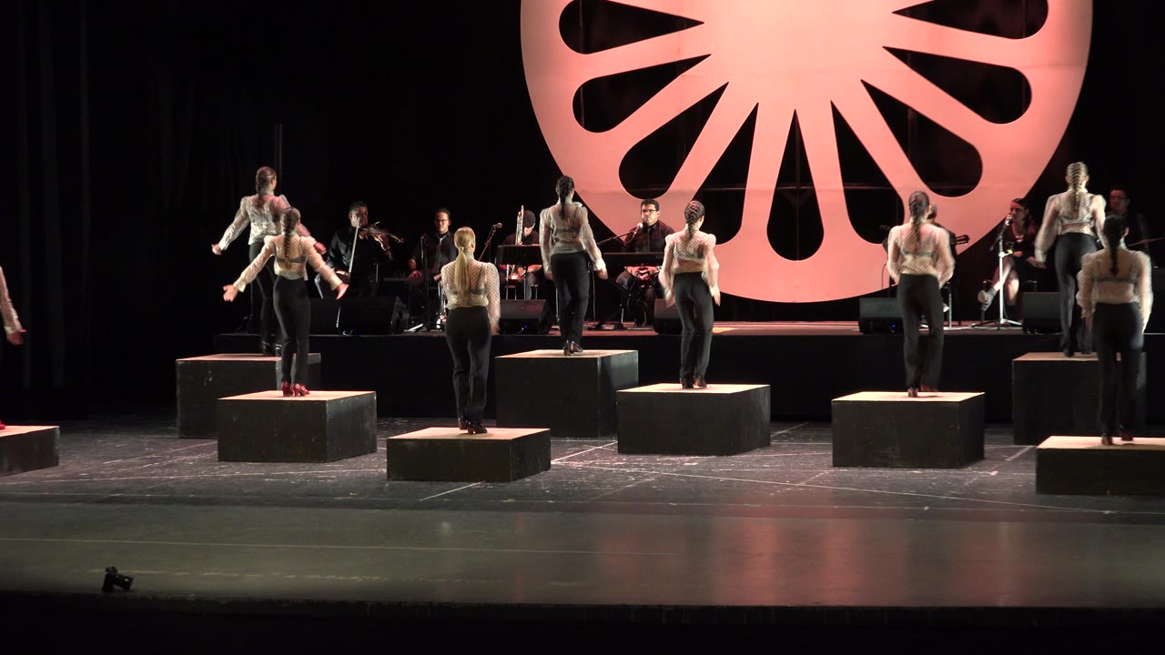 Wide stage view with male dancers on black cube platforms and musicians behind them.