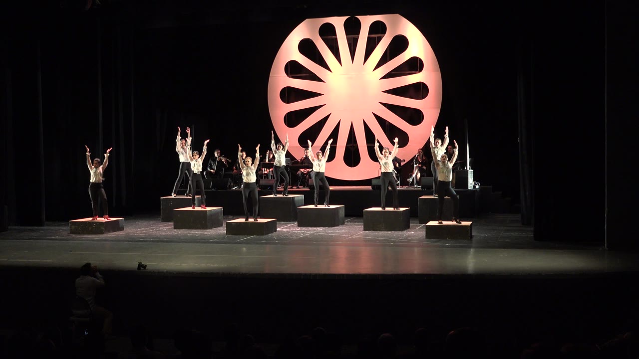 Dancers on platforms under a glowing circular stage backdrop.