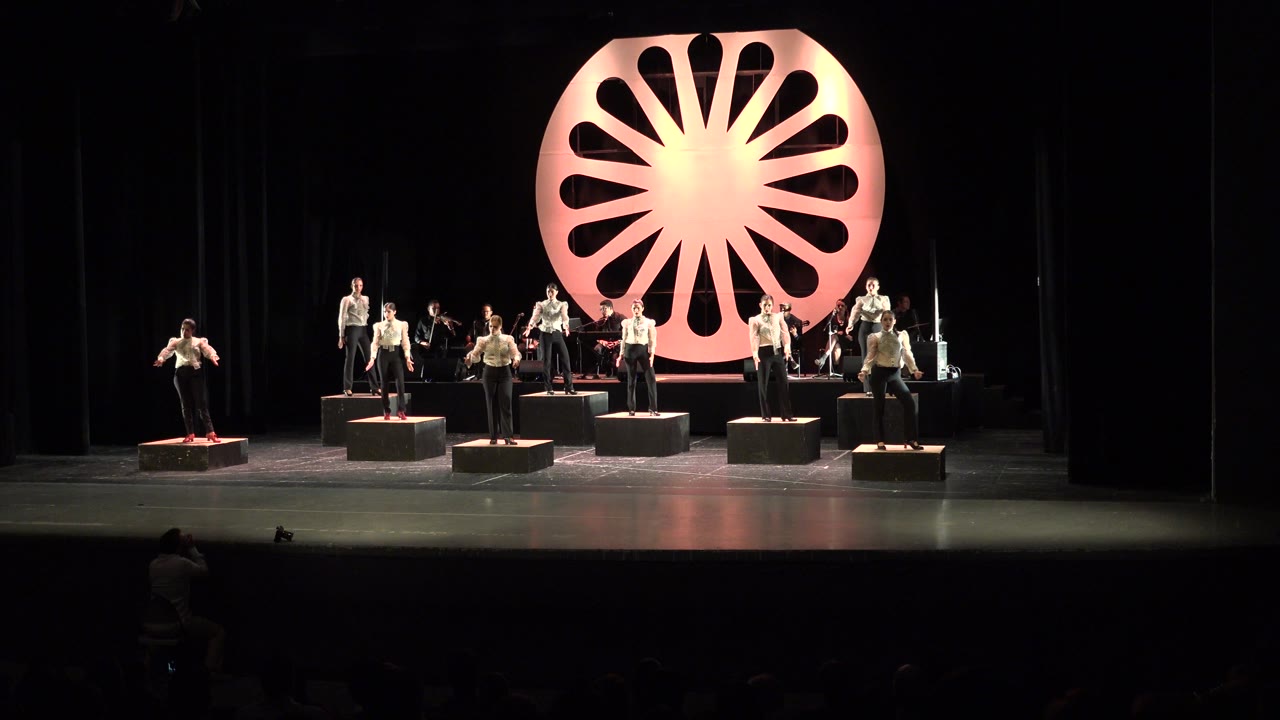 Cabo San Lucas performance frame with the dancers still arranged across separate platforms while the warm circular backdrop dominates the rear of the stage.