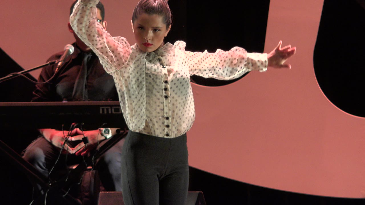 Young dancer holds one arm high and one arm extended across the stage.