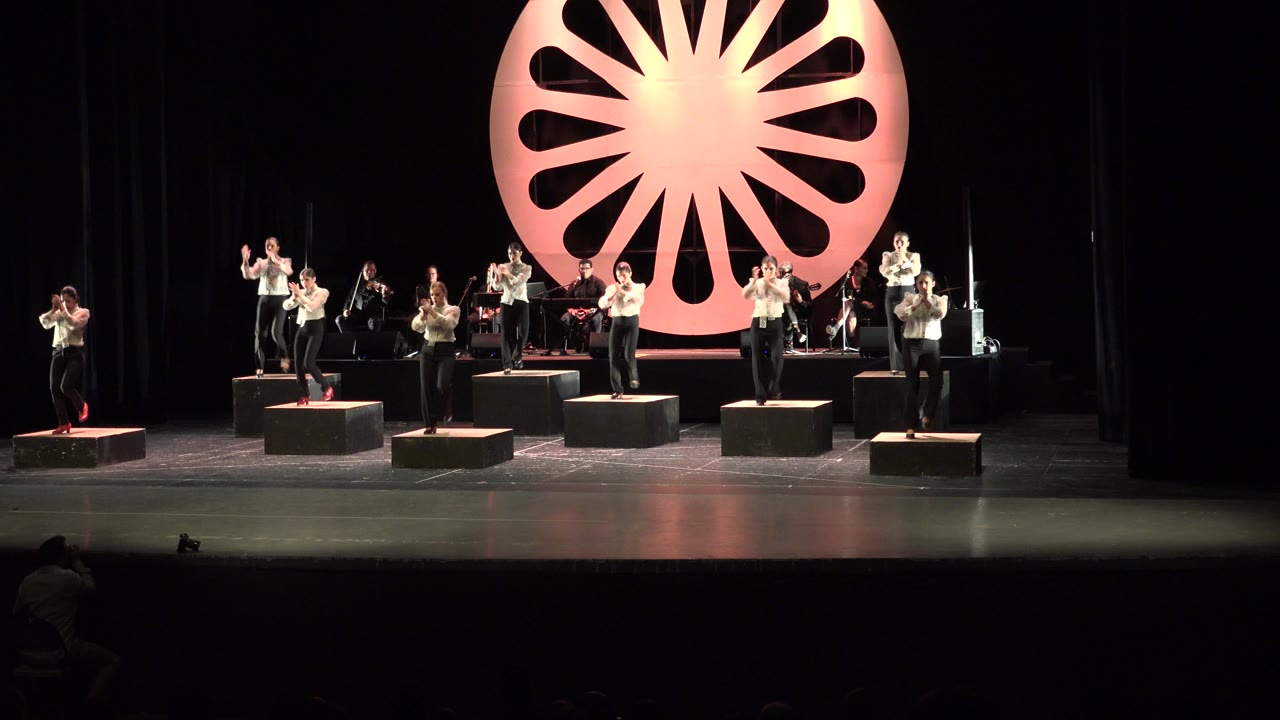 River dancers continue in formation across a dark stage with a warm orange backdrop.