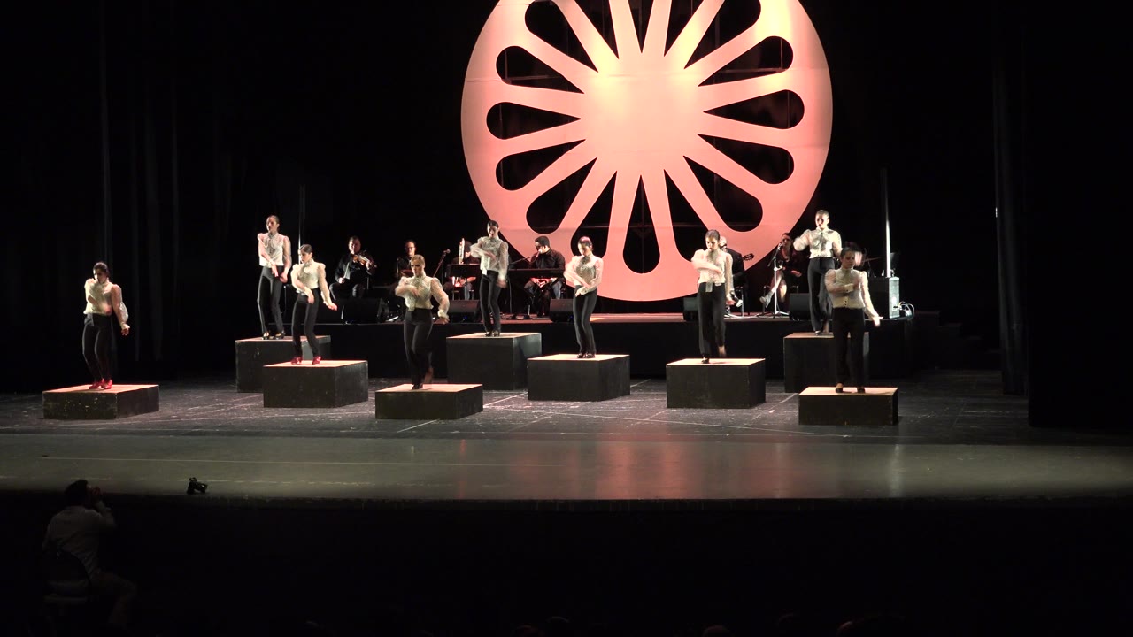 Wide theater stage with women on platforms and musicians behind them.