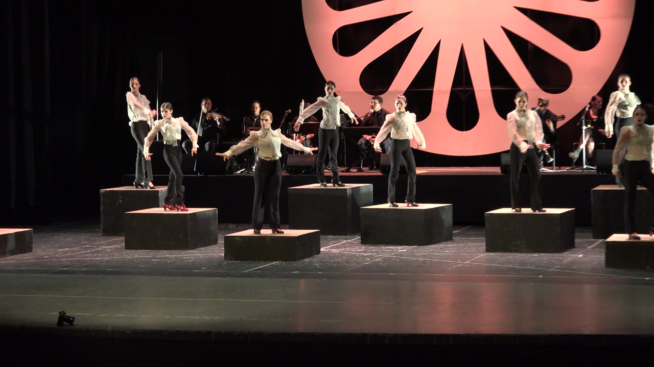 Wide stage view with performers standing on black cubes and musicians behind them.