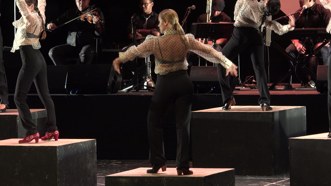 Dancers extend arms while performing on stage blocks
